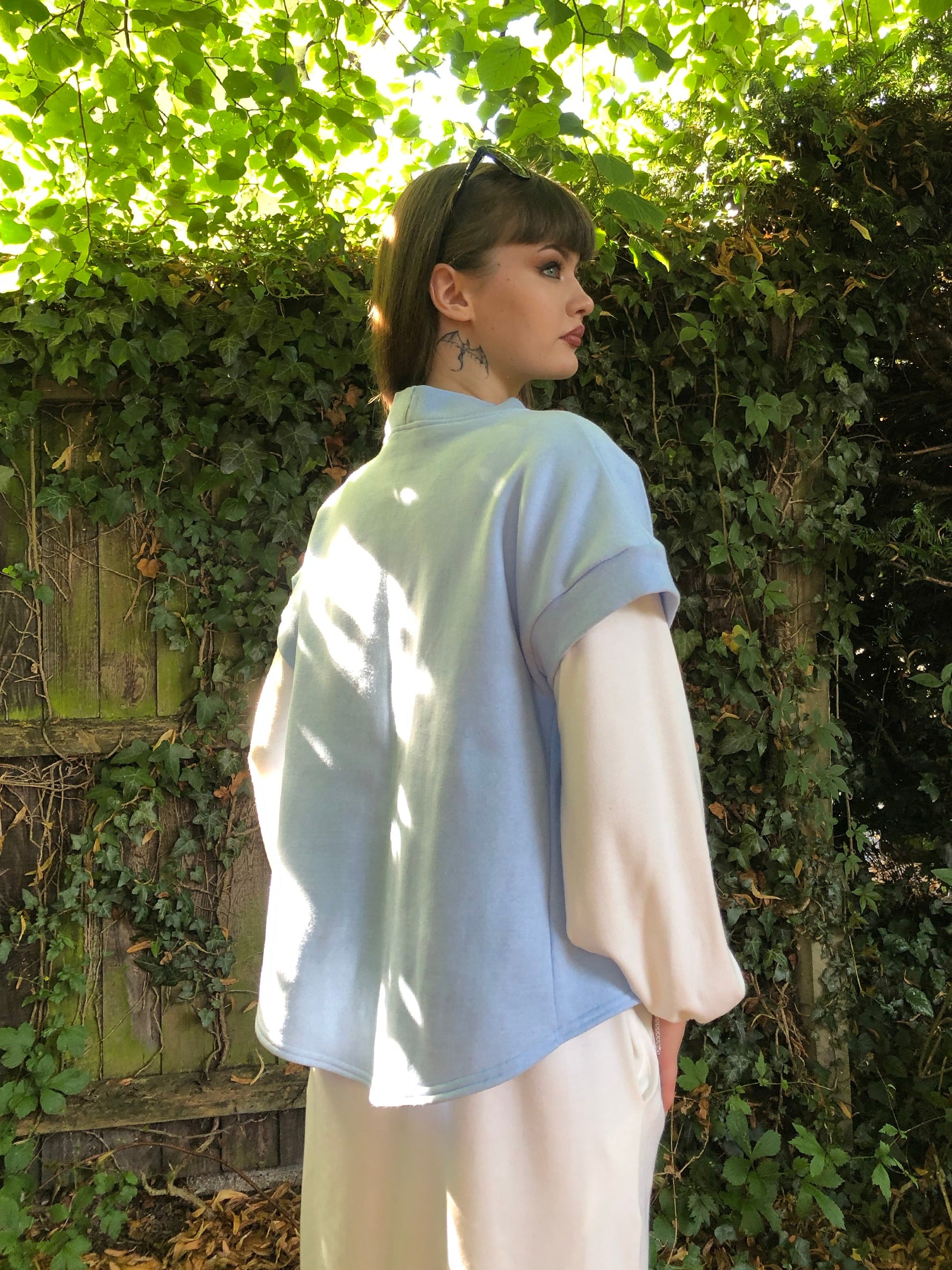 Here our model with brown hair is wearing the Signature Twilight Shrug in Baby Blue on top of the Meander Dress in Winter White. Paired with Beige trainers