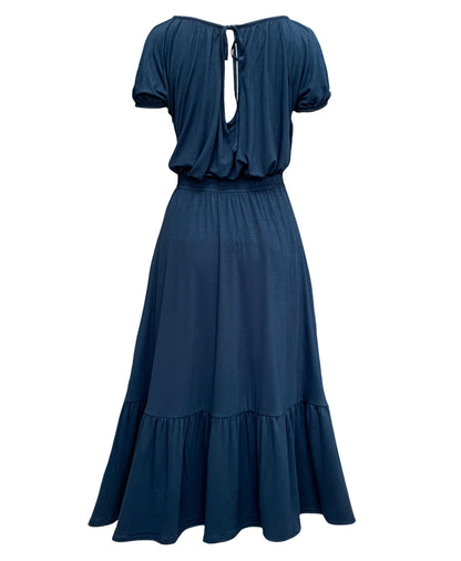 This is a french navy jersey skirt silhouetted against a white background. The skirt has a gathered elasticated waist and deep gathered hem frill. This is a back veiw and tucked in to the skirt is a top in the same colour. It has a keyhole at the back with a gathered neckline and neck tie. It is a loose shape and has short gathered sleeves.