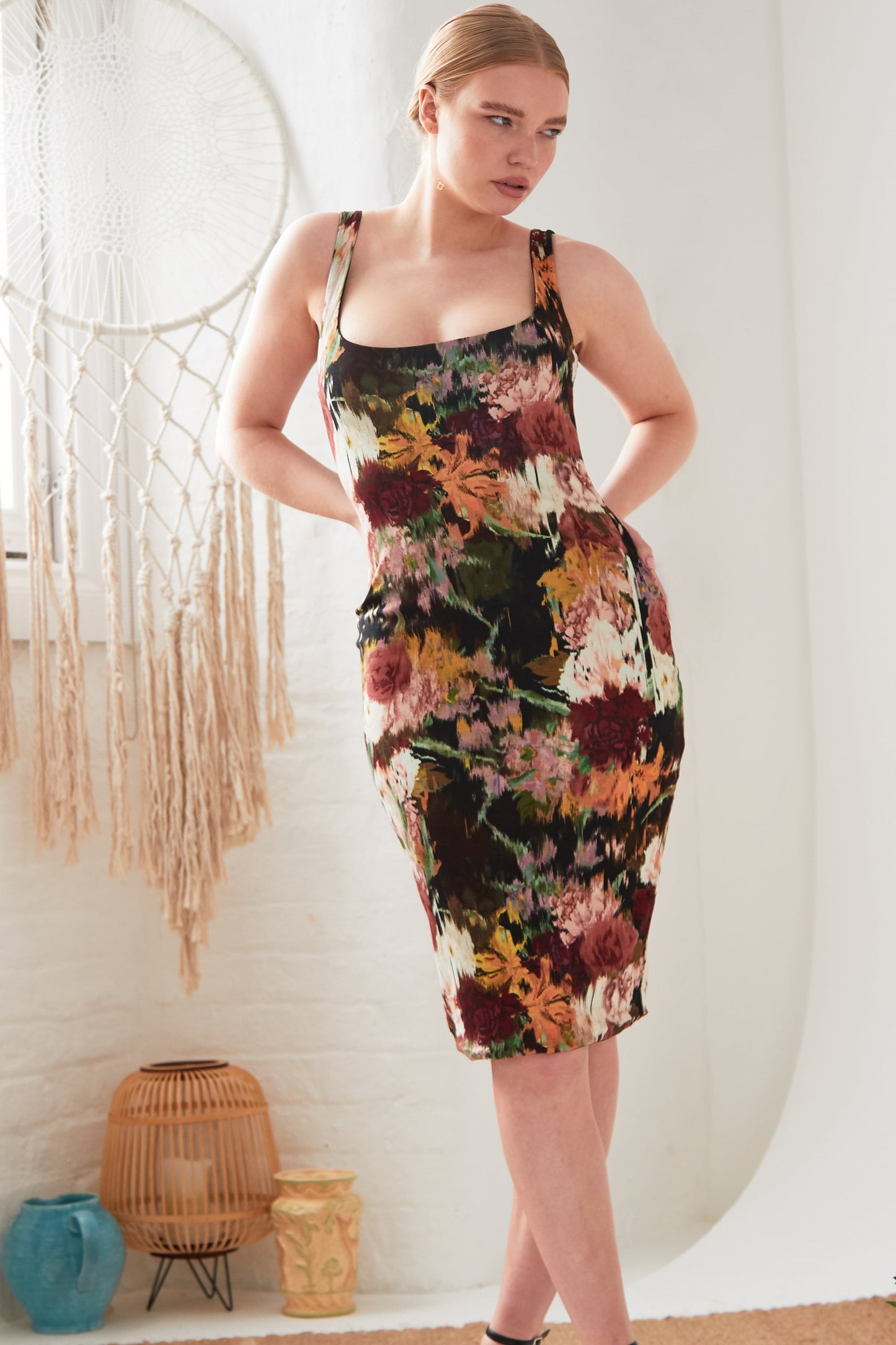 A woman in a Sarvin Sleeveless Floral Bodycon Dress posing in front of a white wall.