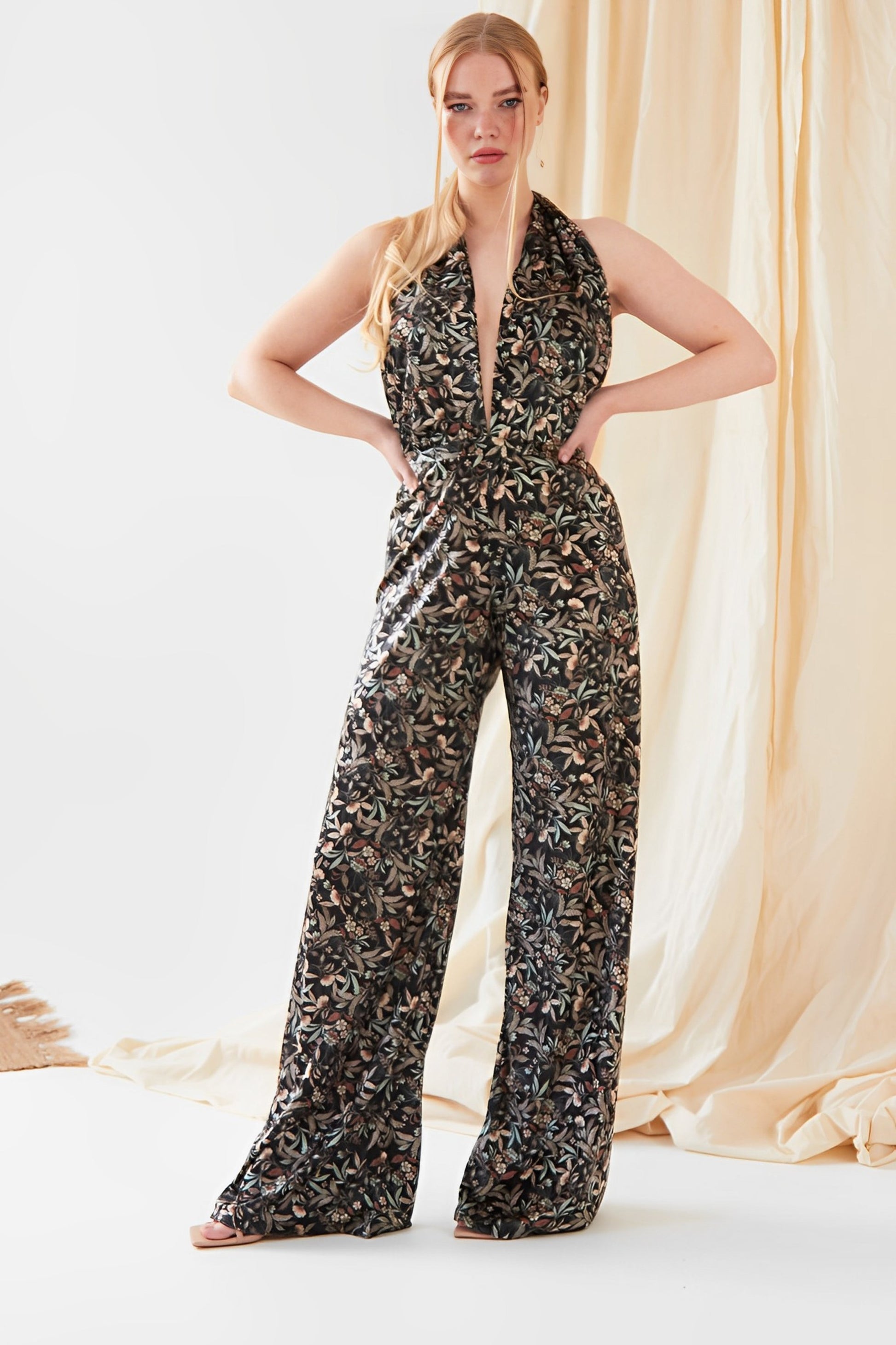 The model is wearing a black Floral Velvet Backless Jumpsuit from Sarvin.