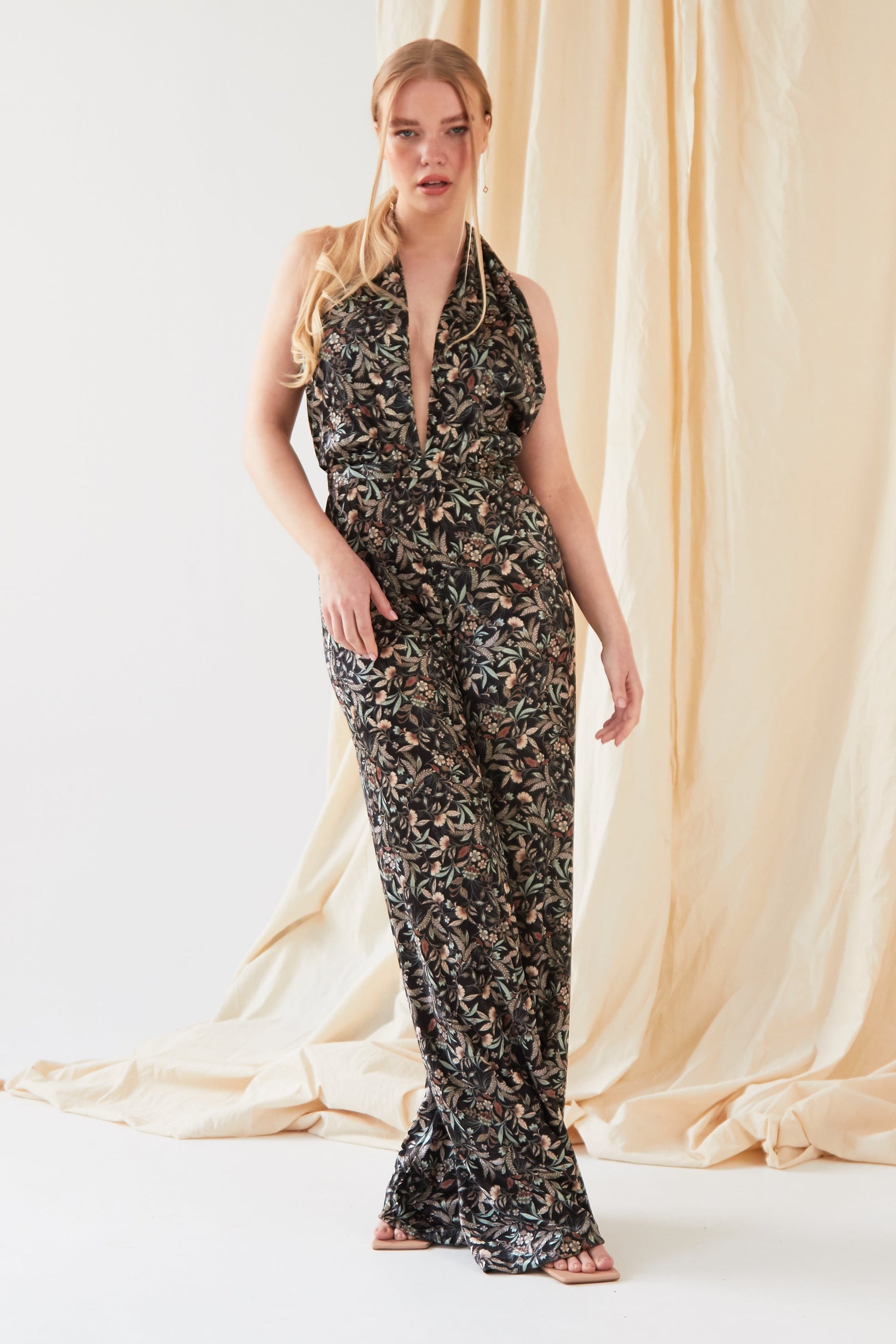 The model is wearing a Sarvin Floral Velvet Backless Jumpsuit.