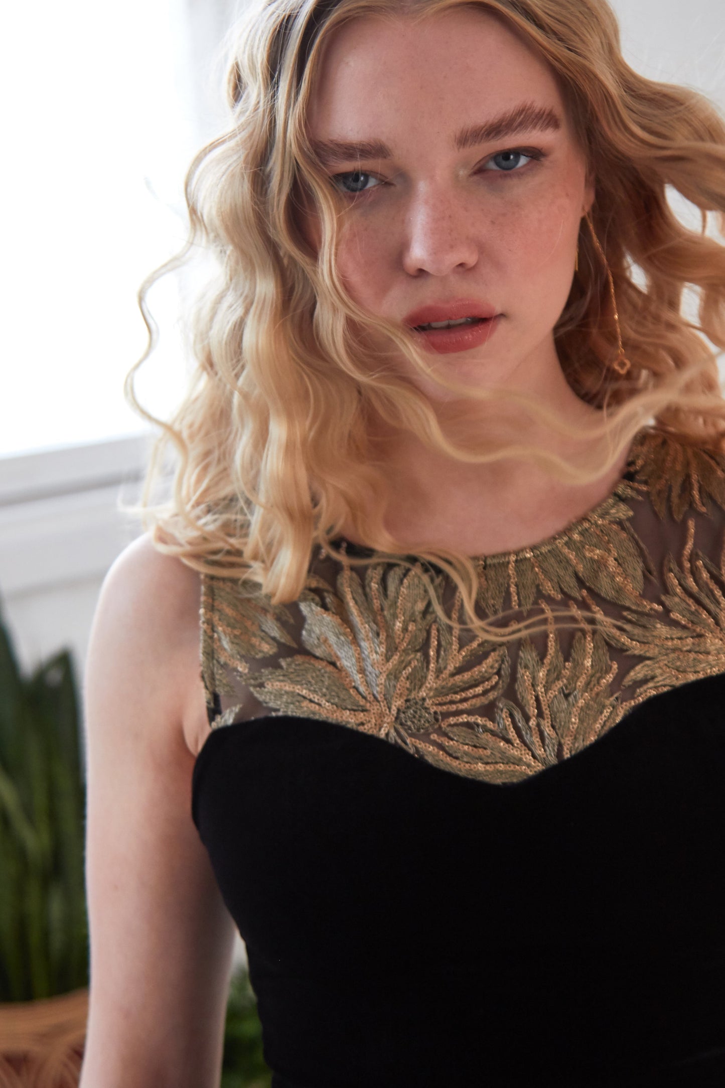 A woman in a black dress posing in front of a window wearing Sarvin's Clover Drop Earrings in Gold.