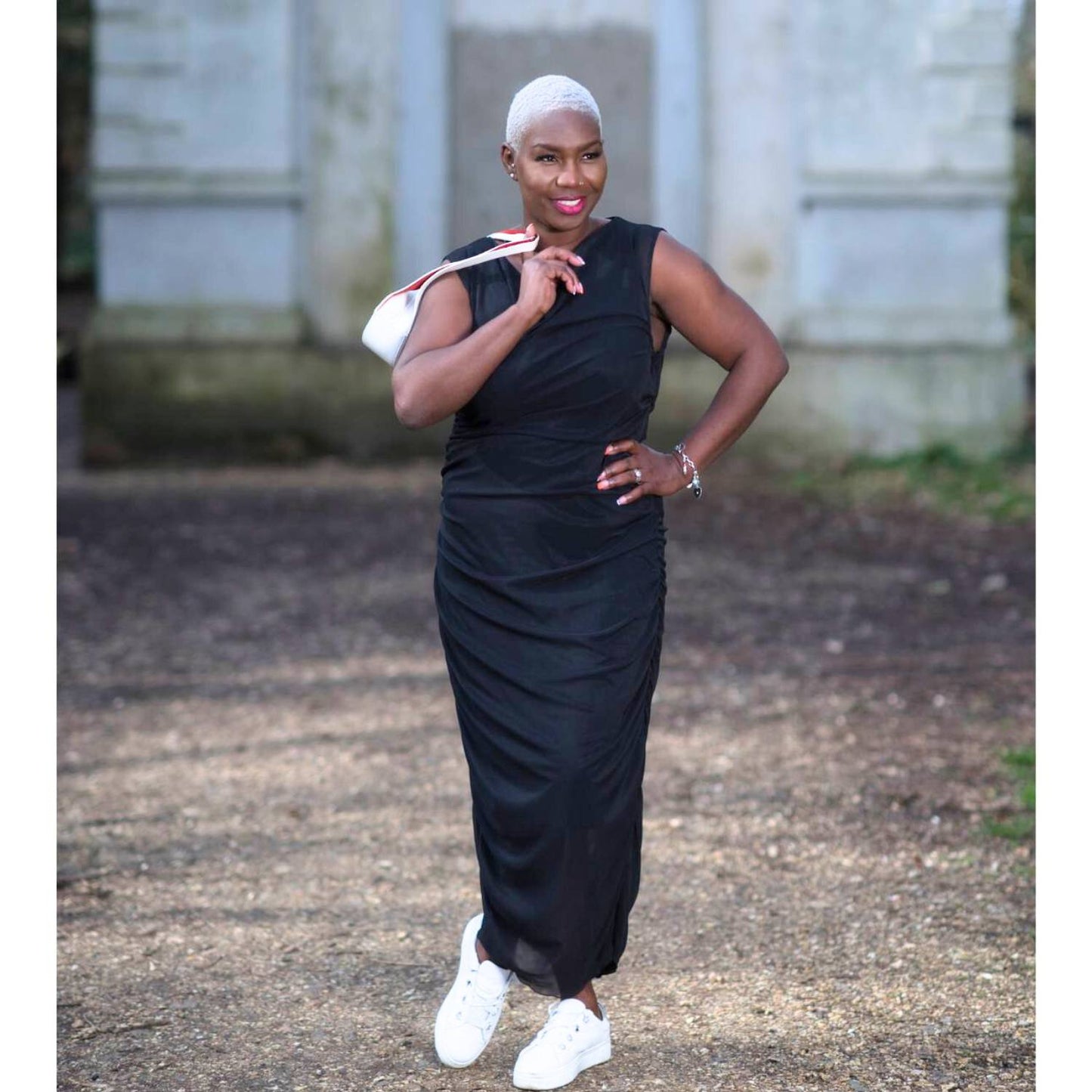 Women's Boudicca Summer Black Ruched Bodycon dress styled with a white handbag and white sneakers for a chic, modern ensemble.