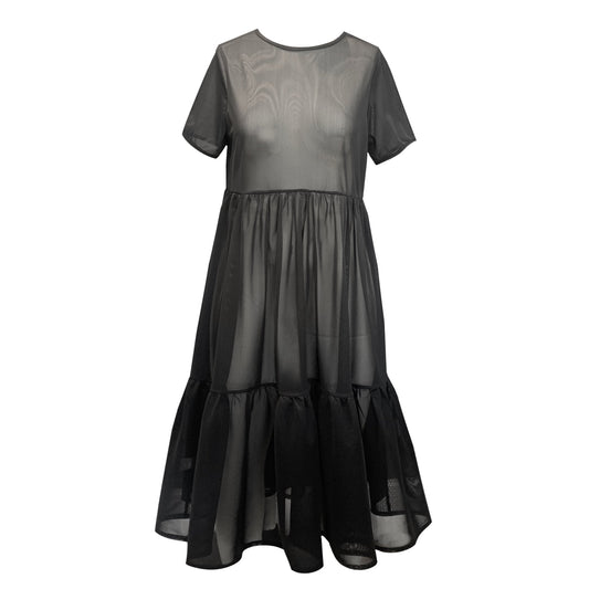 This is a black mesh dress silhouetted against a white background. It has short sleeves and crew neck. There are waist gathers leading to a full skirt which has a deep gathered frill. This is a sheer dress, midi length.